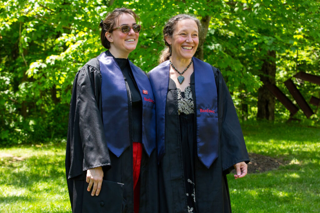 Two BardBac grads in robes with sashes smiling at commencement.